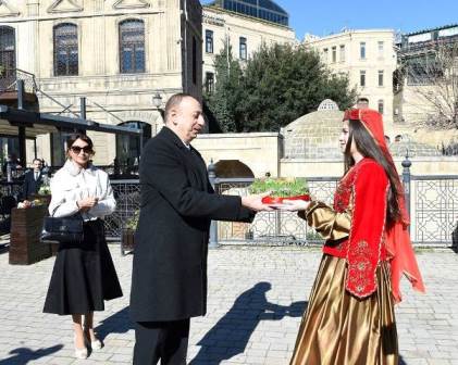 یک زن جوان ارانی سبزه ای را به الهام علی اف ، رئیس جمهور جمهوری آذربایجان پیشکش می کند .